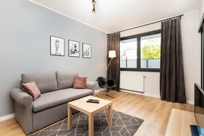 A cozy living room with a gray sofa, coffee table, and floor-to-ceiling windows. The decor is minimalistic, with framed artwork on the walls.