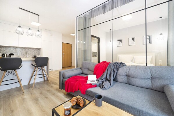 A modern open-plan living space featuring a dining table with chairs, a kitchenette in the background, and a cozy seating area. 