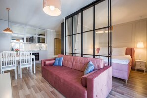 A living space with a table with chair, wooden flooring, and a decorative glass partition that separates the bedroom area from the rest of the room.