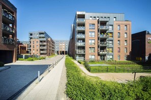  An exterior view of a modern residential complex, with a lush green courtyard area. The buildings are contemporary in design, with brick and glass facades.