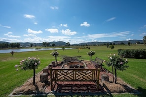 A large, elevated fire pit near the house provides warmth on cooler evenings, with expansive views overlooking the dam and rolling hills.