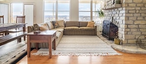Huge windows for natural light and a big sectional surrounds the stone fireplace