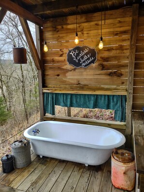 The outdoor bathhouse has an antique tub, large shower, and sink 