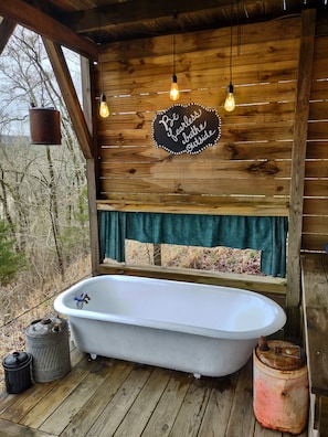 The outdoor bathhouse has an antique tub, large shower, and sink 