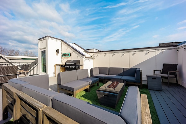 Stunning rooftop deck with multiple lounge areas, fire pit, smart TV, BBQ grill, and dining area.