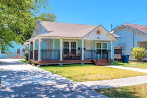 Nestled in a coastal oasis, this abode boasts a light blue façade accented with crisp white trim, evoking a serene beach ambiance. The inviting porch, adorned with four chairs and a quaint table, beckons for leisurely moments amidst the sea breeze. Meandering along a gravel path enveloped by verdant foliage, tranquility reigns supreme, offering a harmonious sanctuary in tune wi...