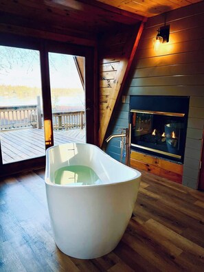 Soaking tub in master bath with views of the water and a fireplace. Cozy!