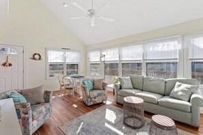The living room features bright, coastal colors and a wall of windows that let in that natural OBX sunlight.
