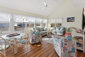 The living room features bright, coastal colors and a wall of windows that let in that natural OBX sunlight.