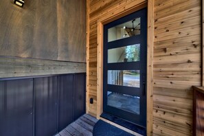 The home's modern-rustic character is introduced by a custom wood front door with vertical glass inserts, offering both style and natural light at the main entryway.