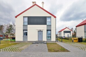 A view of the exterior of a two-story house with a red roof and white walls, surrounded by a driveway and lawn.
