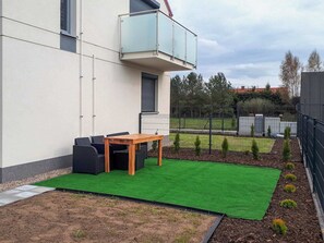An outdoor area featuring a green turf lawn, patio furniture, and pavers, framed by fencing.