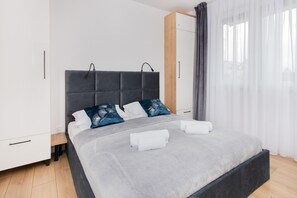 A cozy bedroom showcasing a neatly made bed with gray and blue accents, flanked by matching nightstands and curtains.