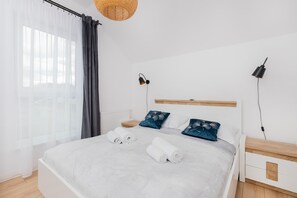 A simple bedroom featuring a double bed with white and blue bedding, bedside tables, and wall-mounted reading lights.