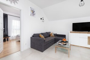 An open living space featuring a gray sofa, a TV stand, and a dining area in the background.
