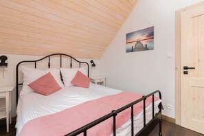 A bright bedroom with a single bed and a bedside table, featuring sloped wooden ceilings.