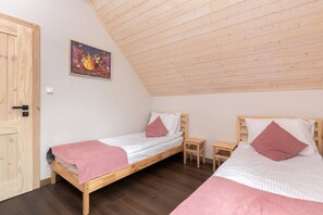 A bedroom with a single bed, pink bedding, and slanted wooden ceilings.