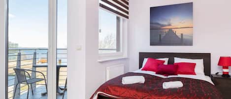 Bright bedroom with a red and white color scheme, large windows, and a cozy double bed.