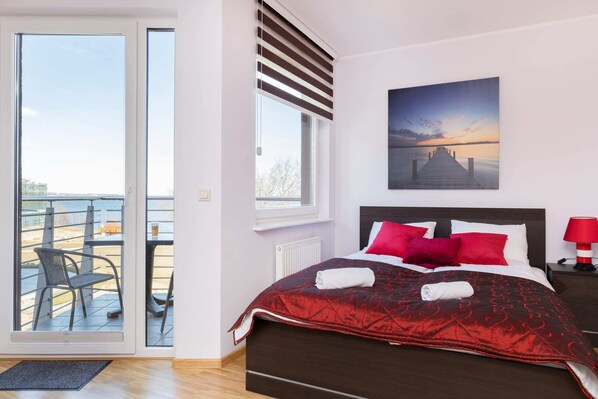 Bright bedroom with a red and white color scheme, large windows, and a cozy double bed.
