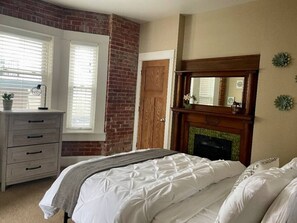 Experience the perfect blend of rustic charm and cozy luxury in our short-term rental's bedroom, featuring an exposed brick wall and a charming fireplace.