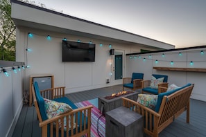 Private rooftop deck with multiple lounge areas, fire pit, and smart TV. Entire deck is outlined by color changing bistro lights.