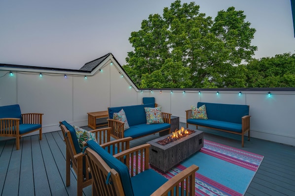 Private rooftop deck with multiple lounge areas, fire pit, and smart TV. Entire deck is outlined by color changing bistro lights.