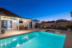 Well lit patio with spa and poolside at night