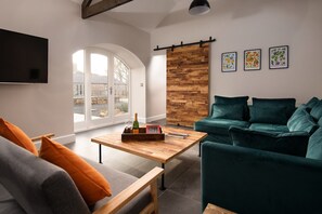 The Steading at West Lyham - TV and bar room with large corner sofa, arch window and door leading to courtyard