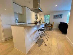 A view of the kitchen with the island and bar stools, and dining table beyond.