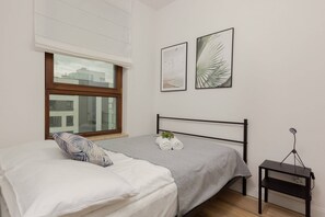 A bedroom with a neatly made bed, minimalist decor, and floor-to-ceiling windows leading to a balcony.