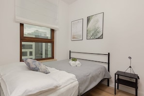 A bedroom with a neatly made bed, minimalist decor, and floor-to-ceiling windows leading to a balcony.