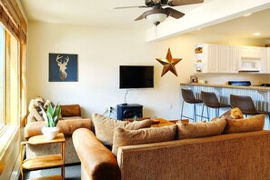 Experience the comfort of our open-concept living area and kitchen, great for socializing and relaxation. The space features a cozy seating area, a smart TV, and a fully equipped kitchen with a breakfast bar for casual dining or morning coffee.