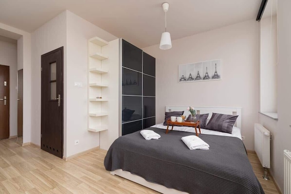 A cozy bedroom featuring a queen-size bed with a gray bedspread, two nightstands, and decorative shelving on the wall.