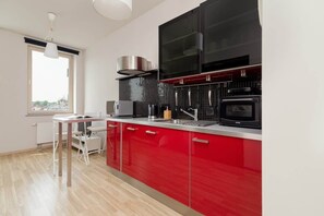 A combined kitchen and living area with red cabinets, a large flat-screen TV, and a spacious layout.