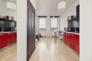 A modern kitchen setup with red cabinets, stainless steel appliances, and a window overlooking the outside.