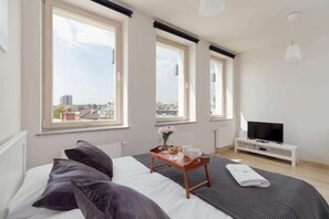 A stylish bedroom featuring a bed with a gray bedspread, a white nightstand, and large windows providing natural light.