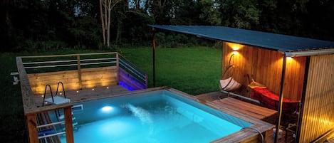 La piscine à la nuit tombée, avec la pergola et ses bains de soleil.