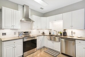 Stainless Kitchen with Farmhouse Sink - This sleek St. Simons kitchen features stainless appliances, granite counters, a deep farmhouse sink, and both a Keurig and Cuisinart—ideal for pre-beach breakfasts before heading to Coast Guard Station Beach or brunch at Mallery Street Café.