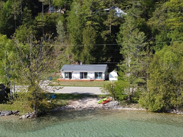 EXTERIOR: A great aerial photo with Crystal Lake, the private beach, lakefront, bonfire ring, and kayaks in the foreground. The cottage itself is in the background.