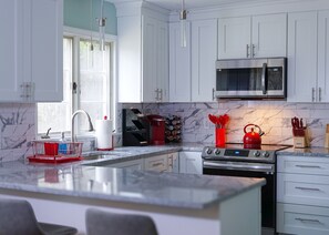 A modern kitchen with a hint of warmth from the red kettle and utensil accents.