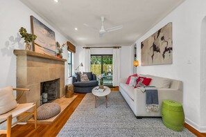 The Living Room combines the original fireplace (non-working) and hardwood floors with comfy seating and a 50" Smart TV. A sliding door opens to the outdoor oasis.