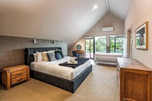 A luxurious upstairs primary bedroom featuring a king bed, freestanding tub, walk-in wardrobe, ensuite, and views of the vineyard.