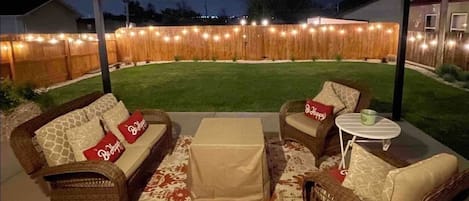 Large covered backyard patio with comfy furniture gas fire pit and cafe lighting