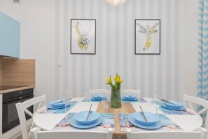 A dining table set with blue tableware and fresh flowers in a vase, placed in a bright area between the living room and kitchen, perfect for meals.