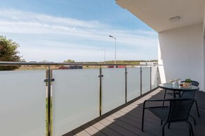 A stylish balcony with glass railing, offering a peaceful outdoor spot with seating for two. The view overlooks the surrounding area, providing a serene space for relaxation.