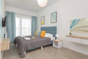 A cozy bedroom with a comfortable bed, soft linens, and decorative yellow and gray pillows. The natural light creates a peaceful, inviting atmosphere.