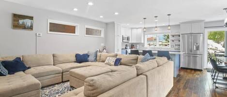 The cozy and stylish, open-concept living, kitchen and dining areas show off the plush and cozy sectional and ottomans as well as the updated kitchen with roomy island, tile backsplash and farmhouse sink.