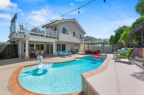 The backyard is a sunny poolside oasis with floaties, BBQ, and cozy seating