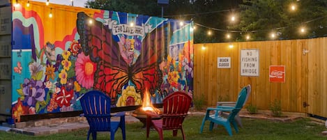 Seating area by art mural with fire pit and string lights on timer