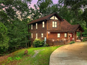 Cabin at sunset, cozy and rustic among the trees with a welcoming circular driveway that promises serenity and seclusion.